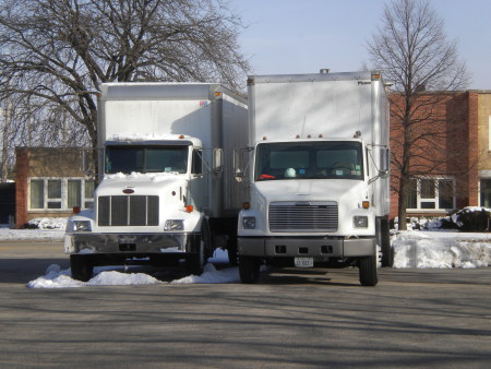 A photo of 2 straight trucks parked in a parking lot.